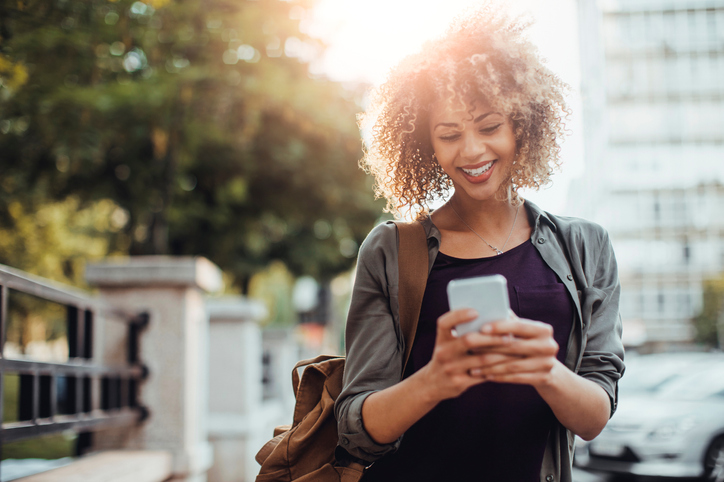 mulher negra de cabelo cacheado sorrindo com um celular na mão