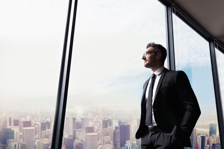 Empresário olhando pela janela do escritório - capital de giro para crescer: qual o momento certo de investir na sua empresa?